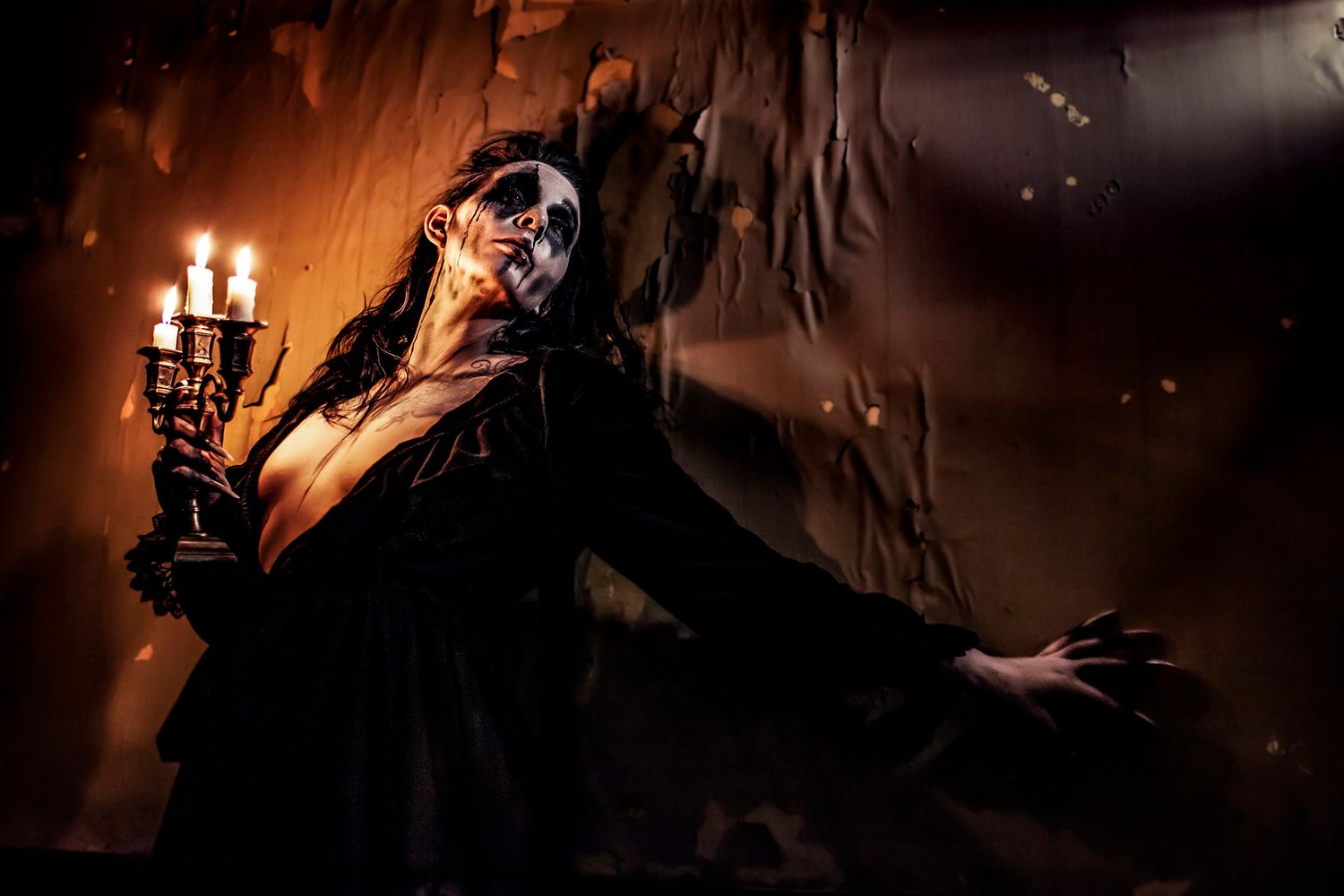 Dramatic figure in gothic makeup and black clothing holds candelabra in dark atmospheric setting with candlelight.