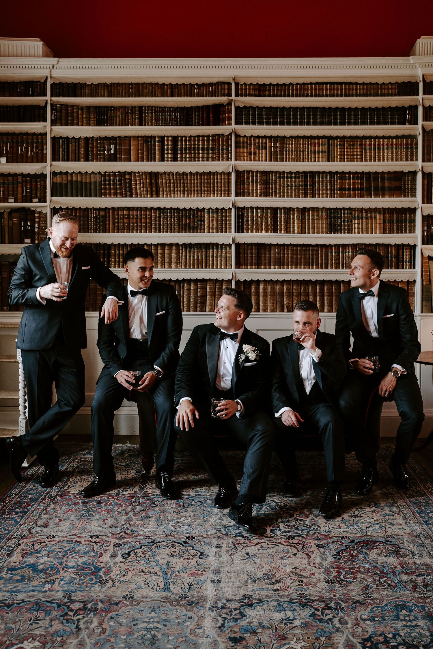 groom and groomsmen sitting on sofa drinking whiskey in the library at Iscoyd park