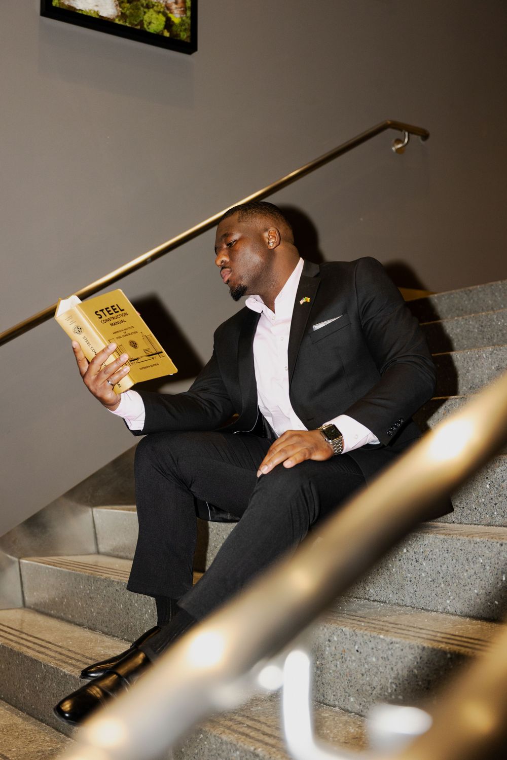 Person in a suit reading a yellow book on modern concrete stairs.