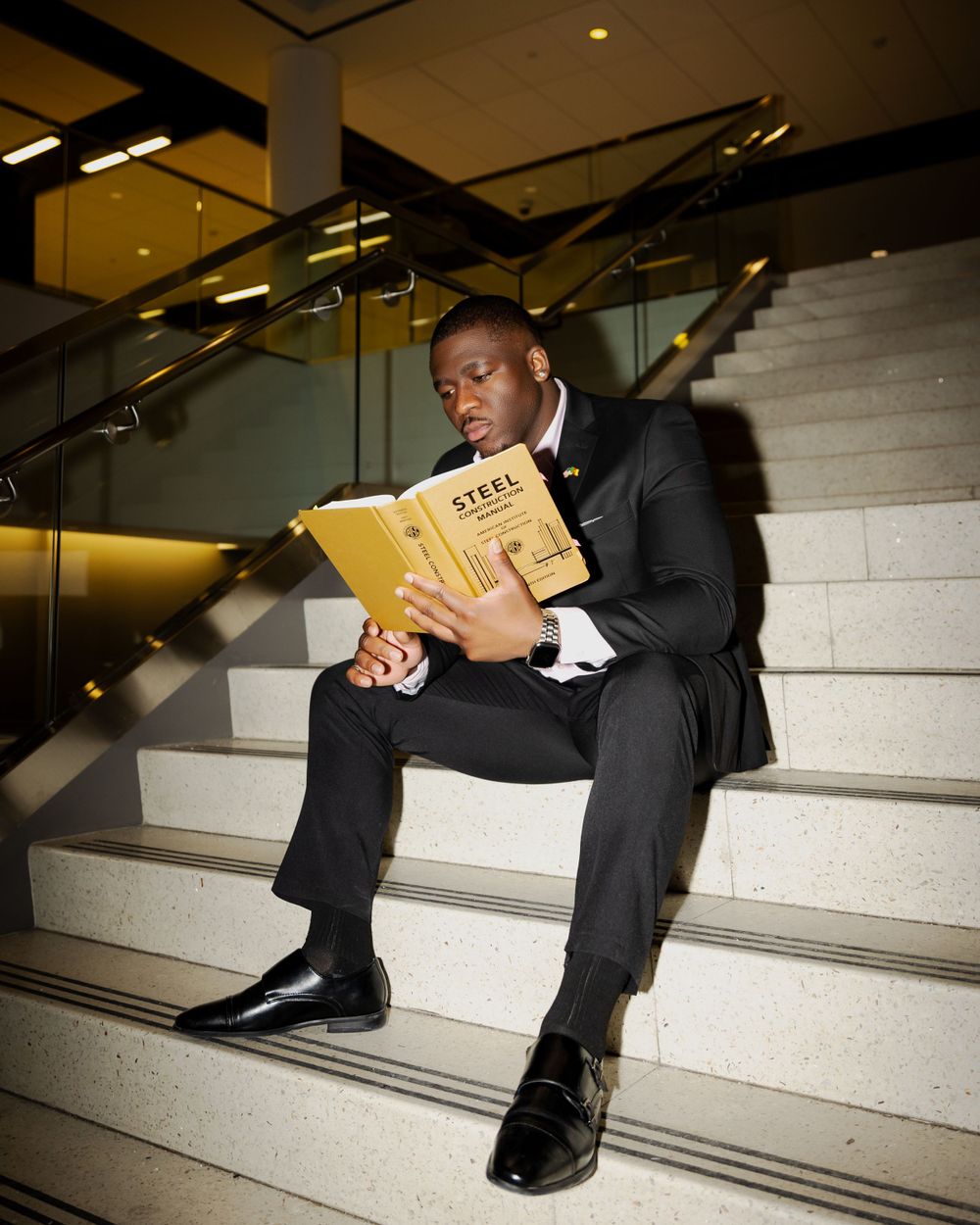 Person in formal attire reading yellow book on white stairs.