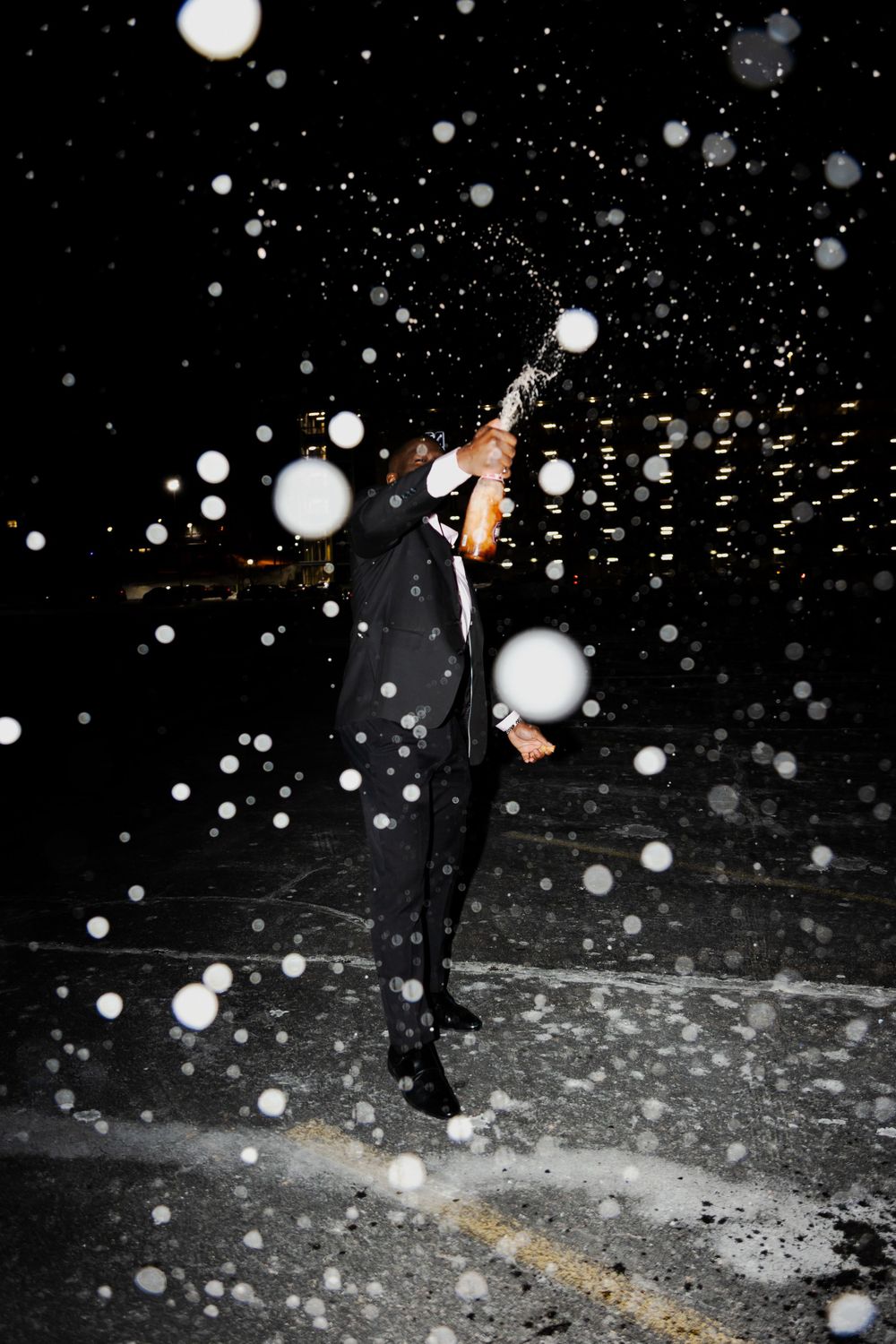 Figure in suit celebrating in snowfall at night.