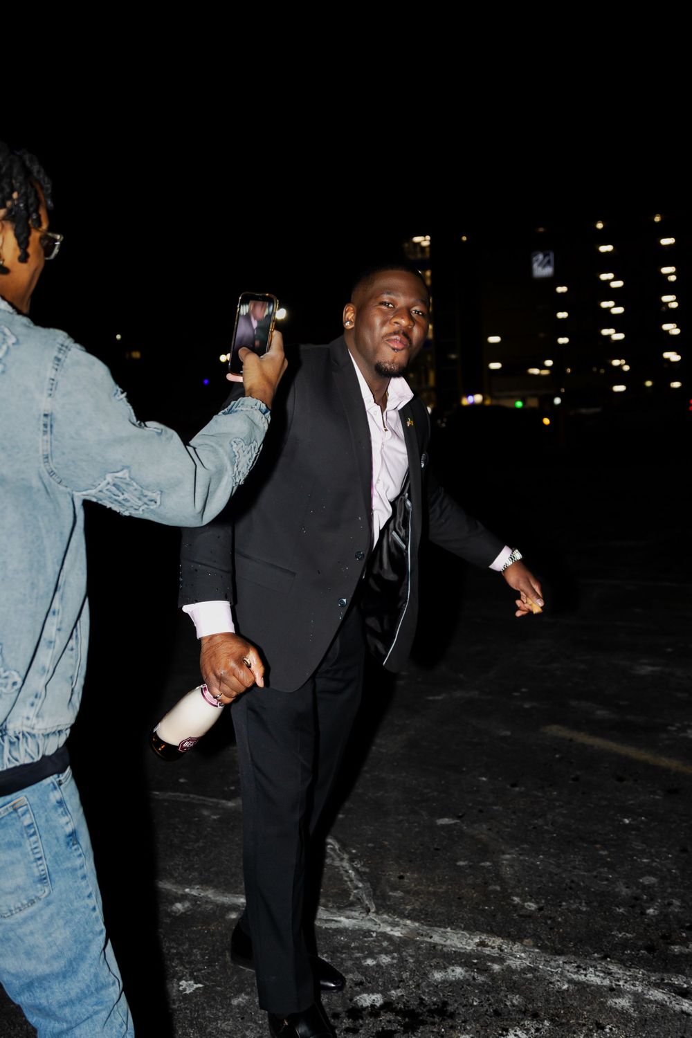 Person in a suit and tie dancing joyfully at night against a dark background.