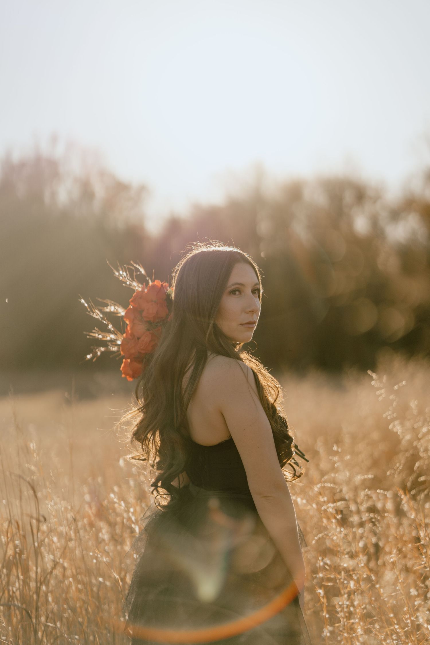 Golden hour portrait in a wheat field with sun flare and flowing hair.