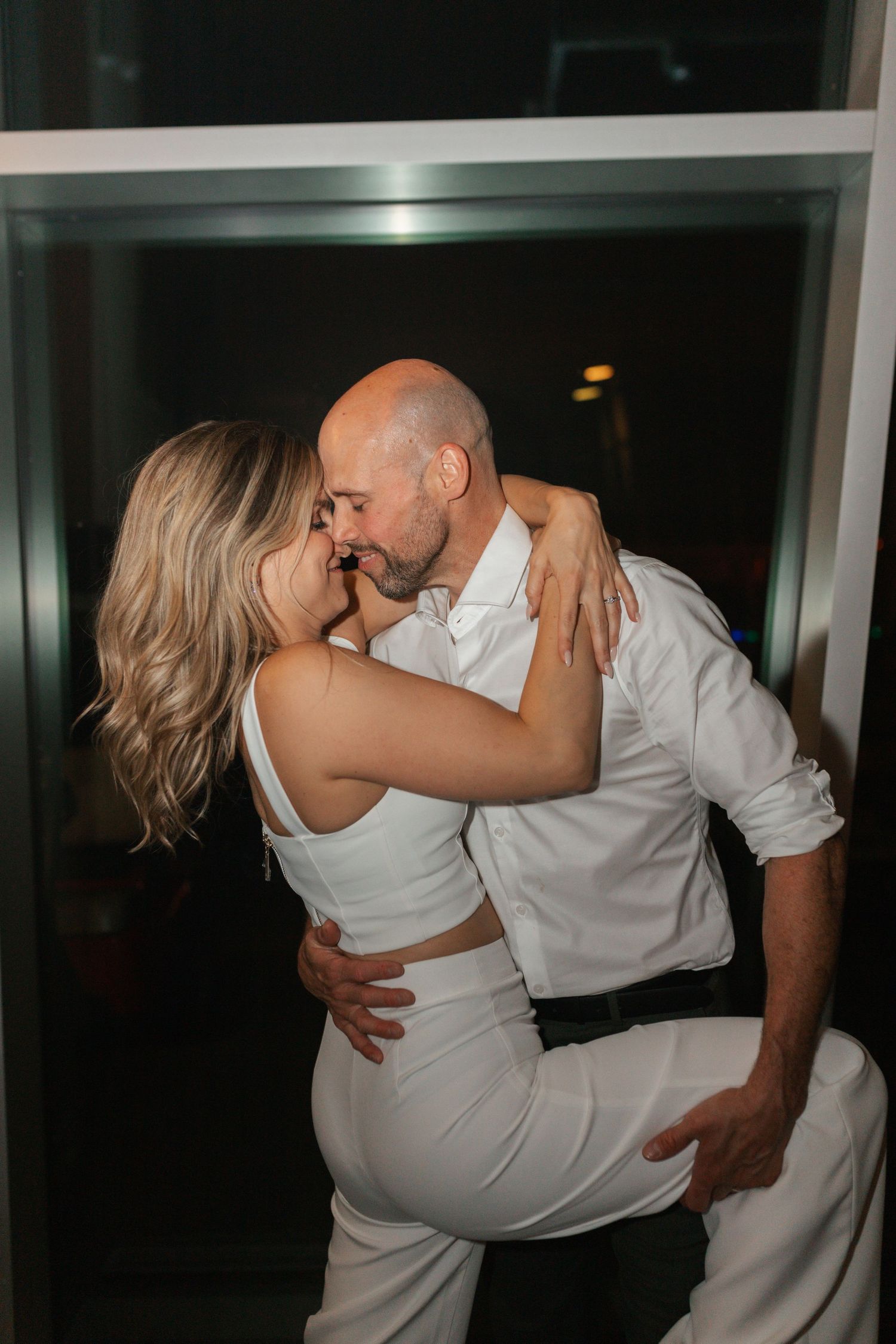 Bride and groom sharing a passionate kiss in a doorway during their wedding reception at night.