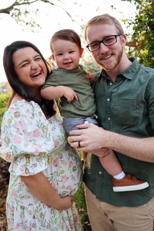 A joyful family portrait outdoors with a toddler wearing green against a natural background with trees.