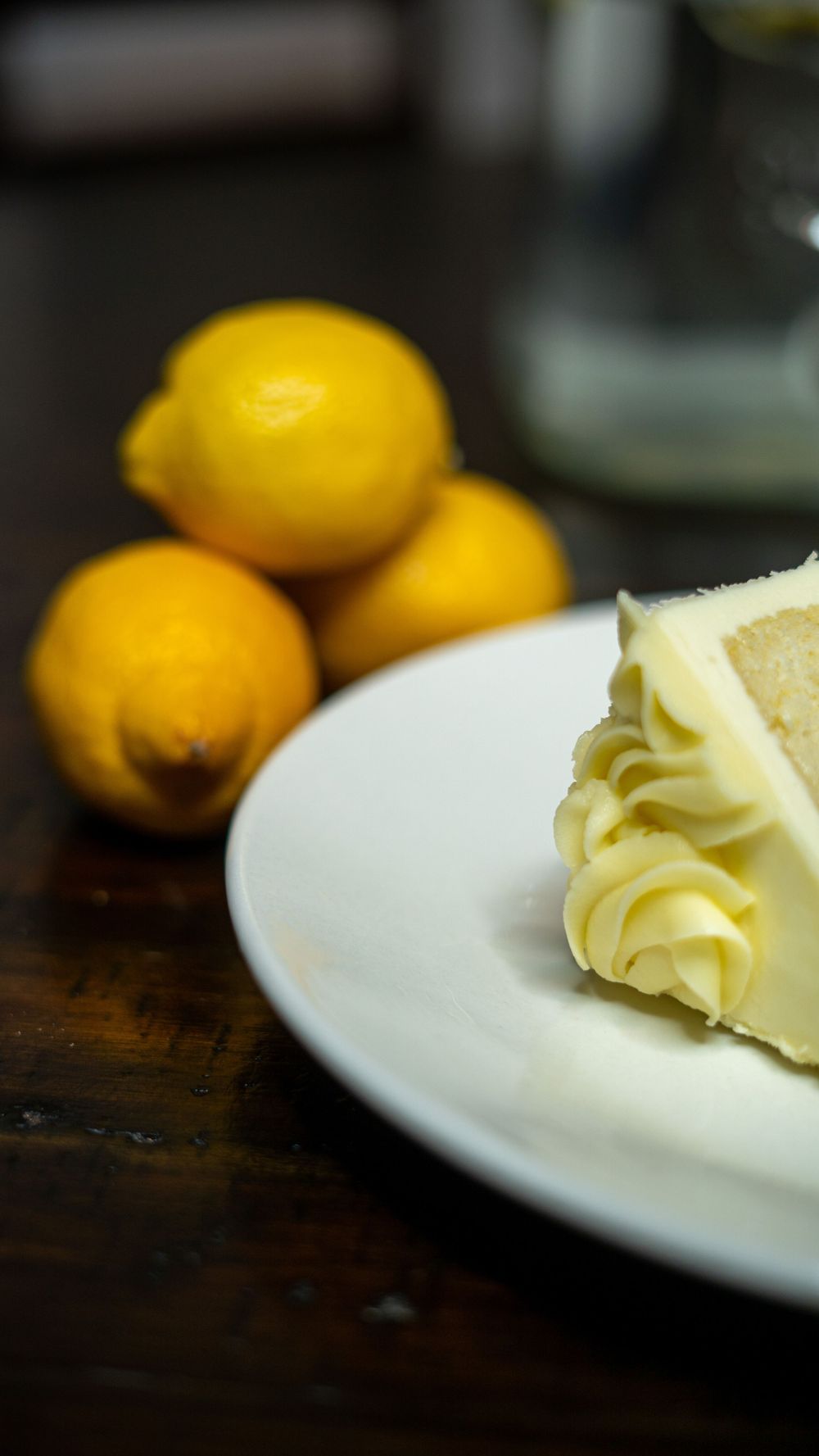 Fresh yellow lemons and a pat of butter on a white plate against a dark wooden surface.
