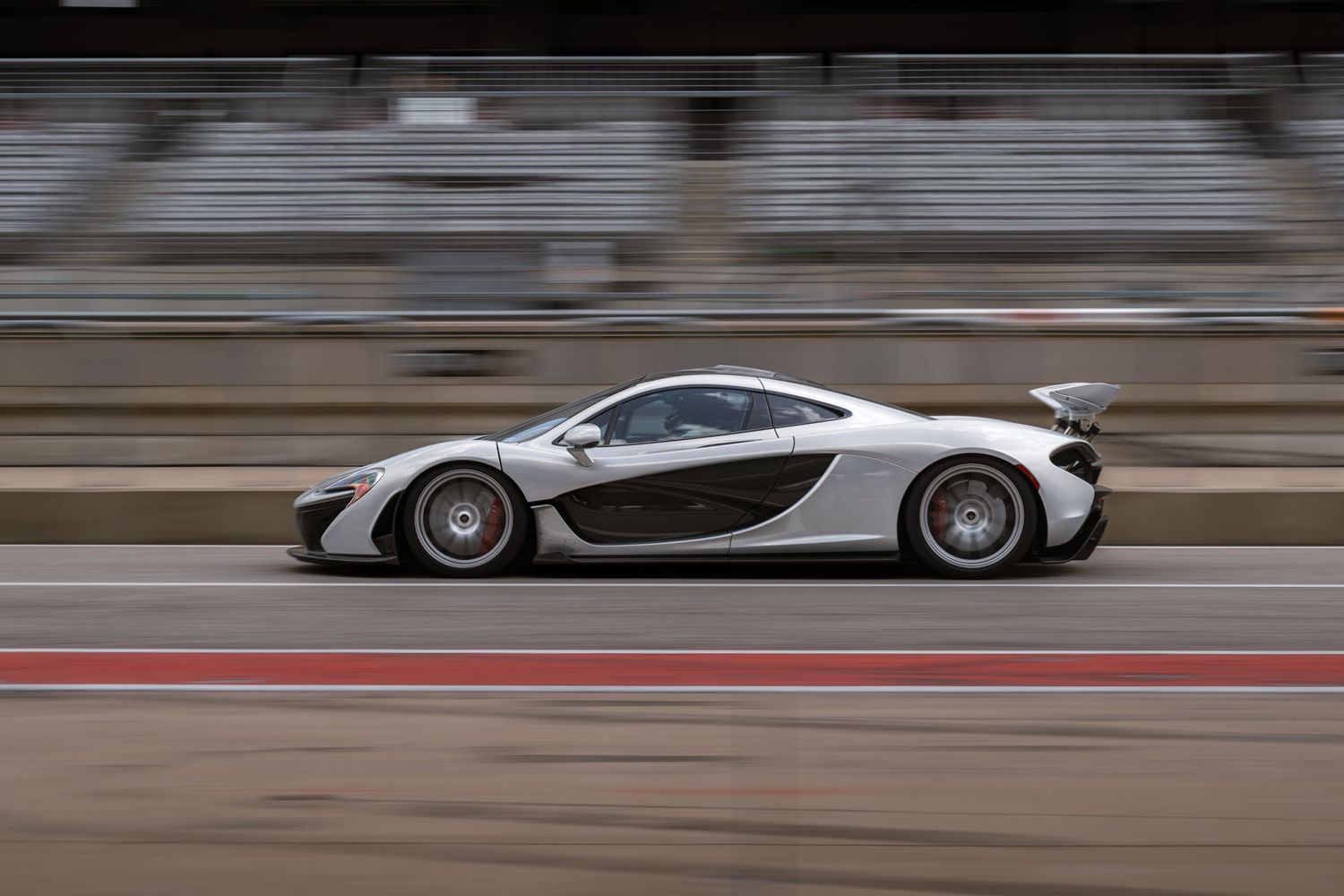 Silver sports car speeding past motion-blurred grandstands on a race track.