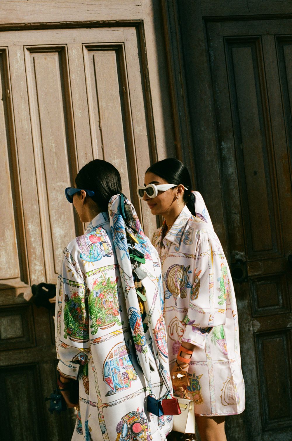 Two people wearing matching printed oversized shirts standing near wooden doors in artistic street style photography.