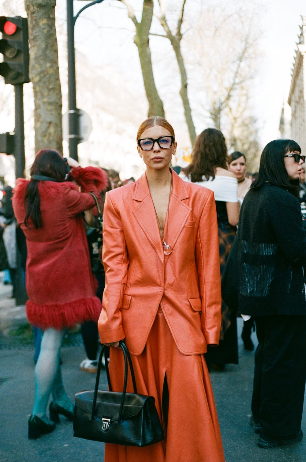 A street style outfit featuring a bright coral-colored pantsuit paired with glasses and a black leather handbag.