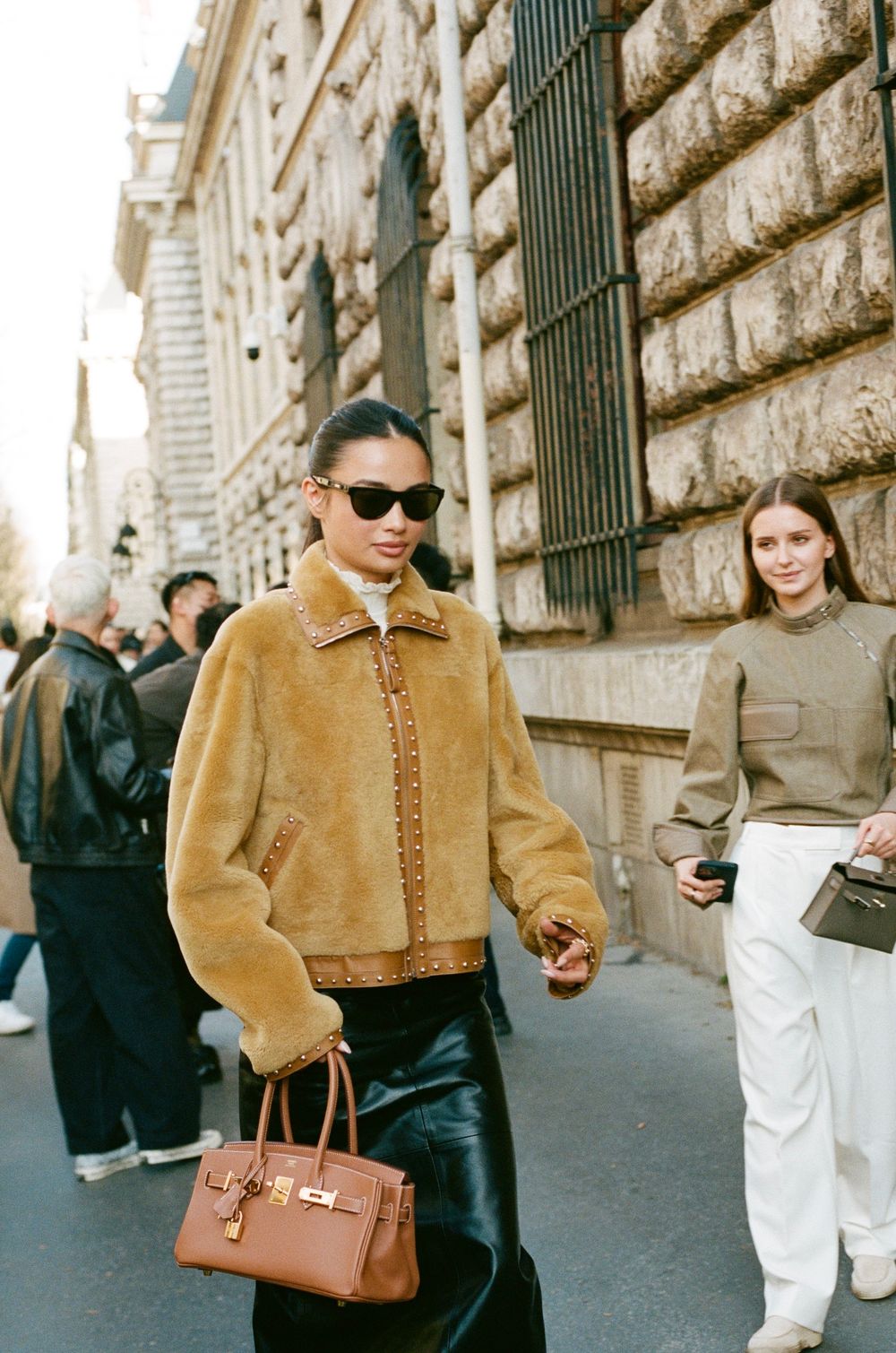 Street style fashion shot showing brown shearling jacket, leather pants and cognac handbag against classic architecture.