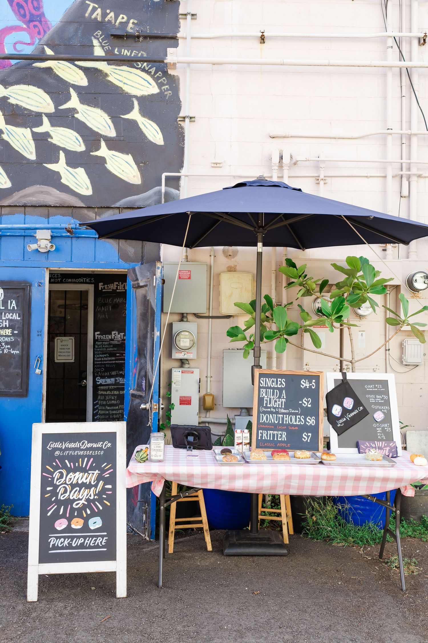 Outdoor cafe setup with blue umbrella, chalkboard menu and blue storefront featuring minimalist street vendor display.