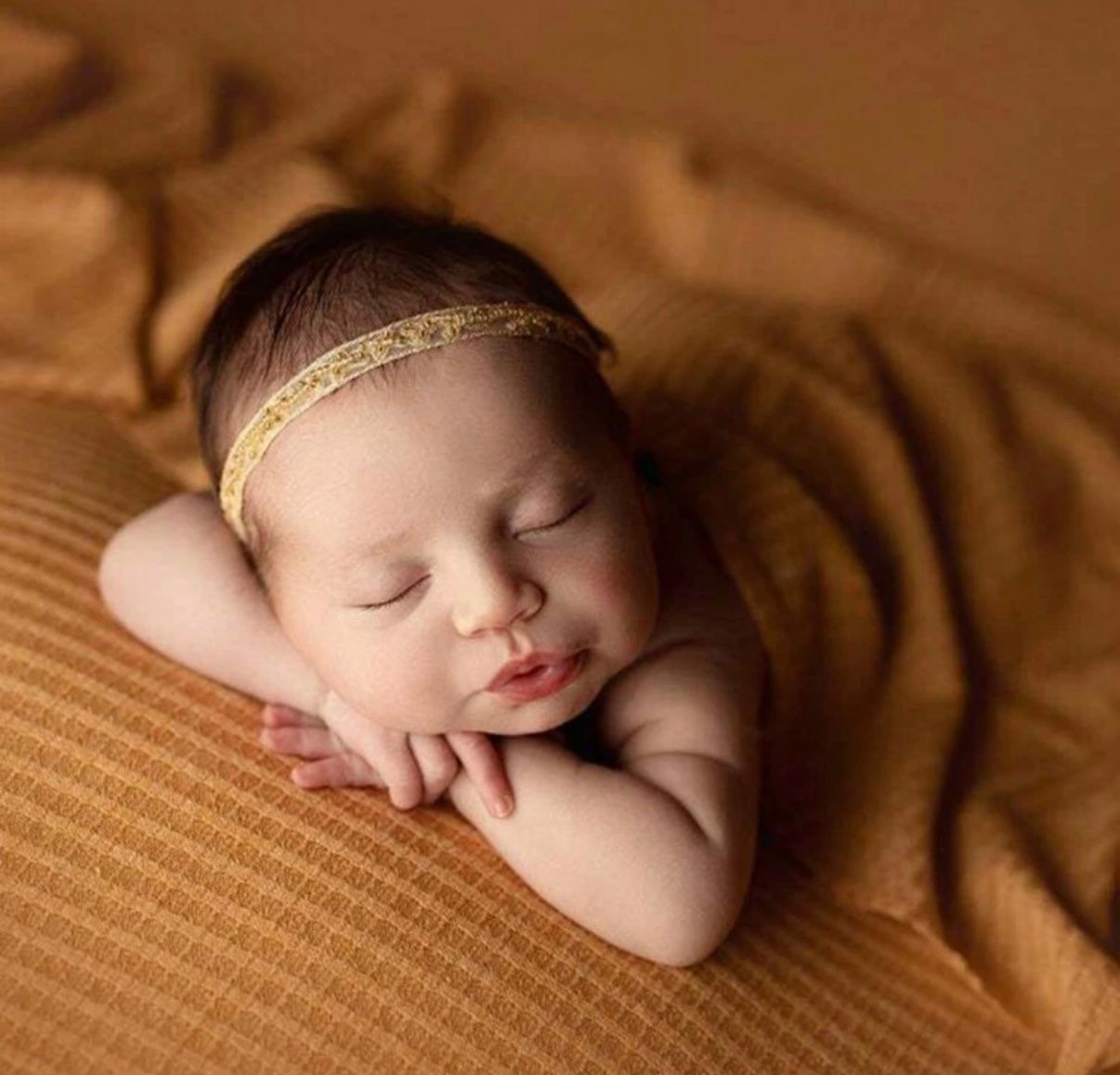 Sleeping newborn on textured brown backdrop with delicate headband.