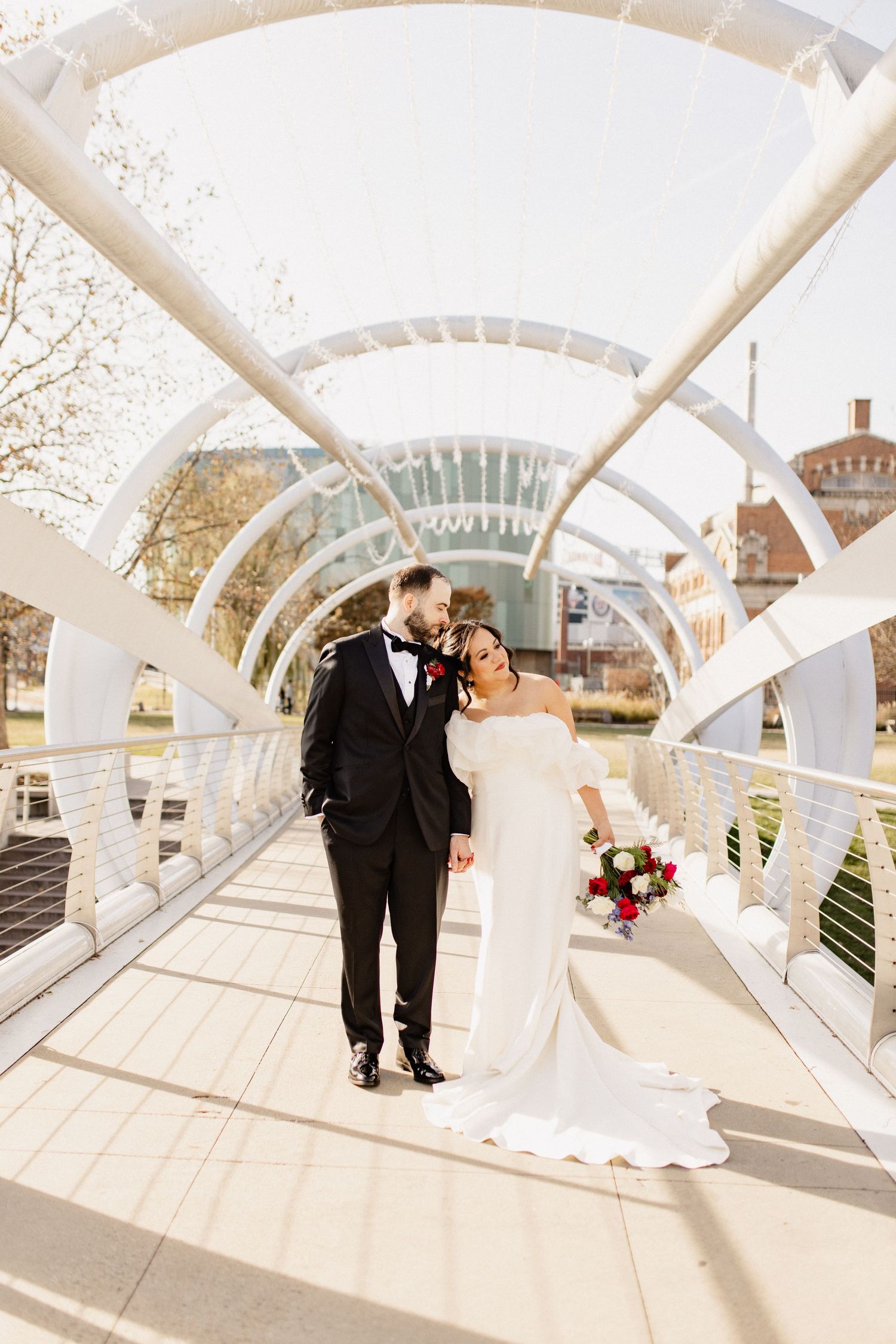 A couple shares a romantic moment on a modern white architectural bridge walkway on their wedding day.