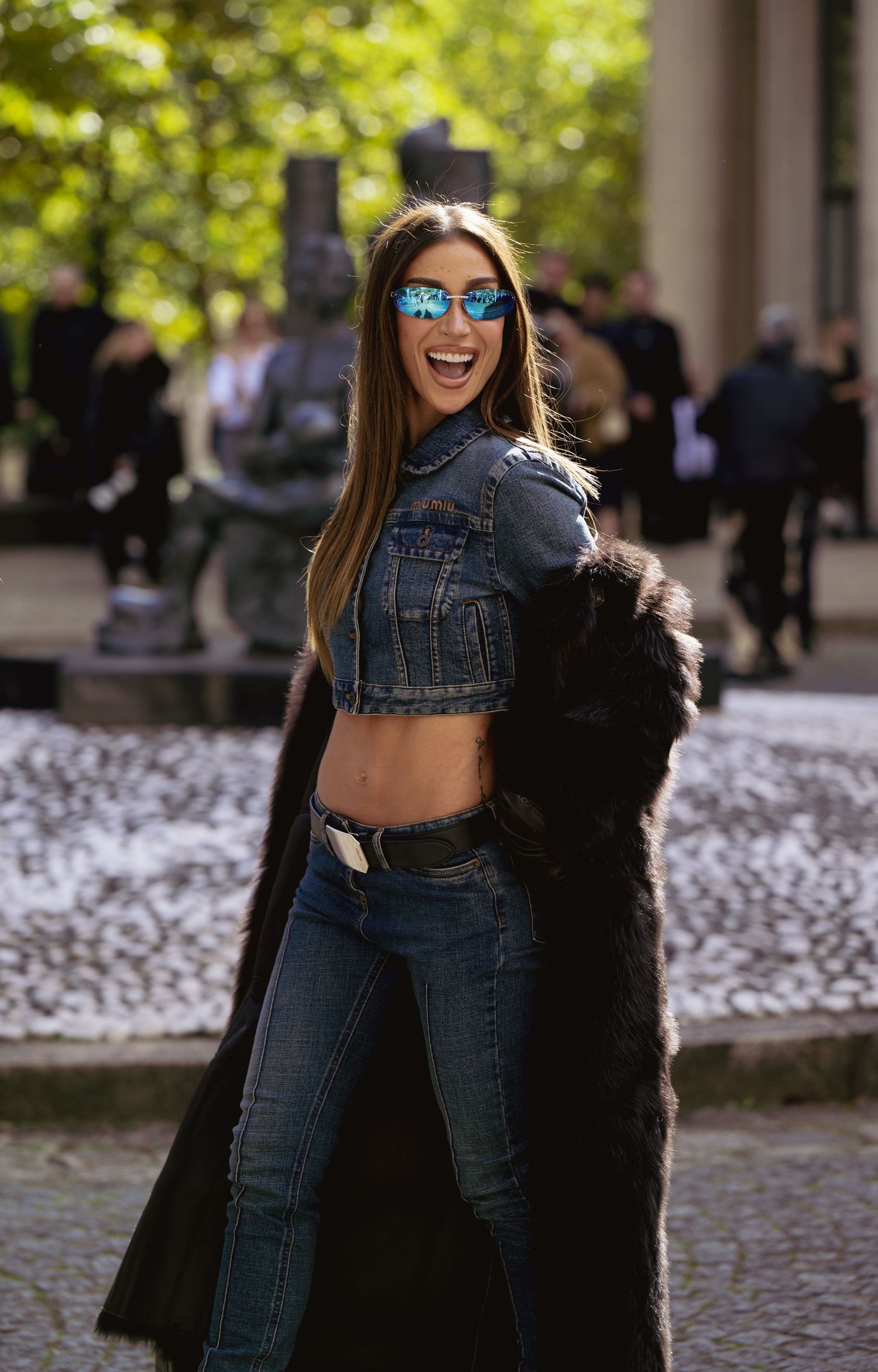 Street style shot featuring cropped denim jacket and long fur coat on cobblestone path.