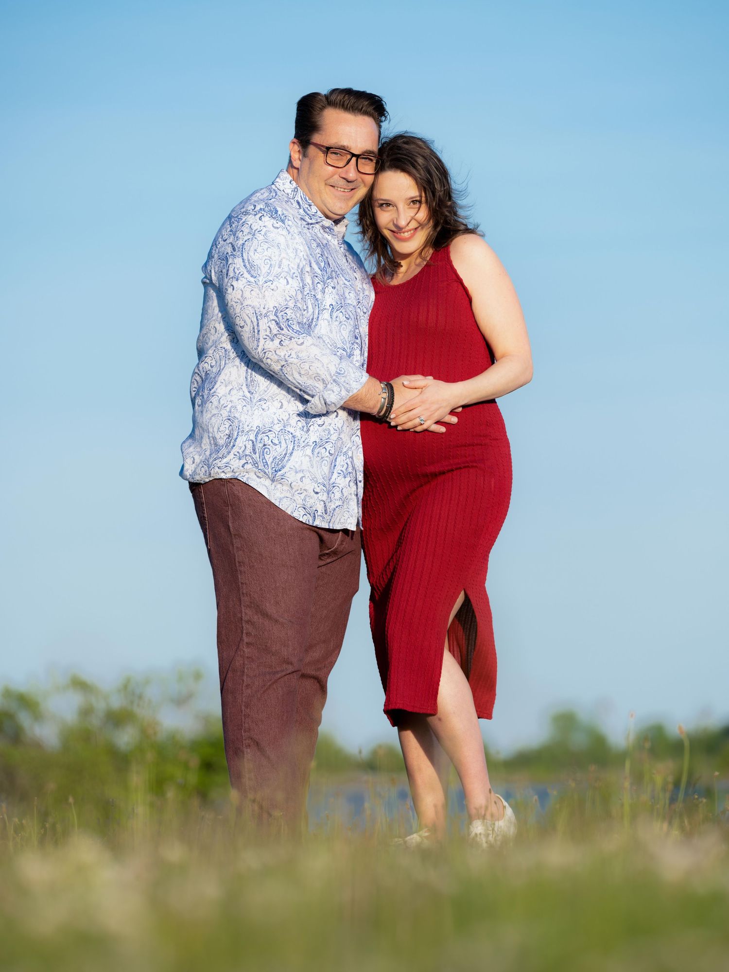 Couple embracing in an outdoor setting against a bright blue sky background.