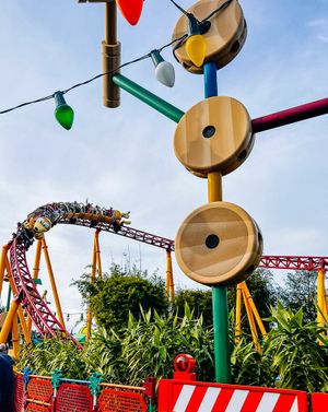 A roller coaster track curves past giant decorative Christmas lights and wooden discs at an amusement park.
