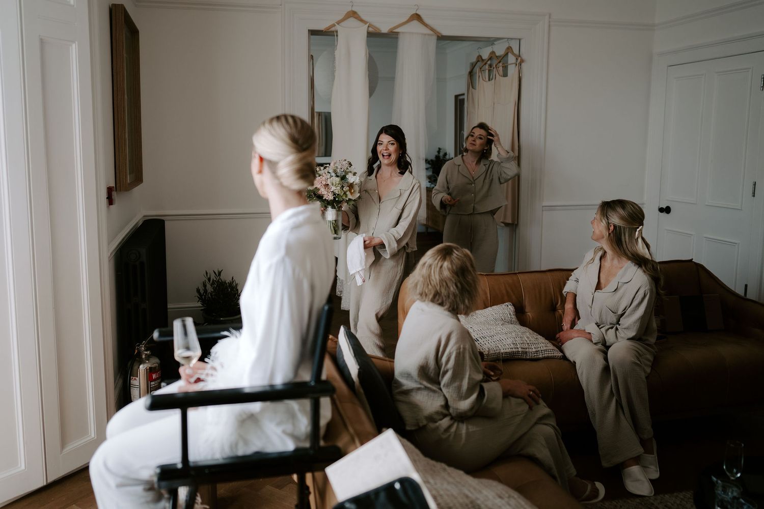 Tunnels Beach Wedding Venue in North Devon, Bride sat in chair getting make up done with bridesmaids carrying bouquet