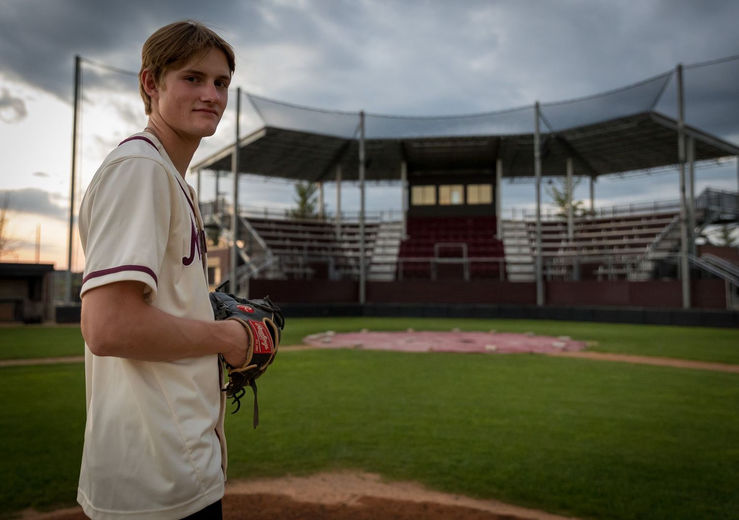 portrait of a young man wearing a baseball jersey and glove standing on the pitching mound facing home plate