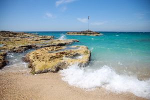 Turquoise waves crash against rocky coastal formations under bright blue skies at a beach in Batroun, Lebanon.