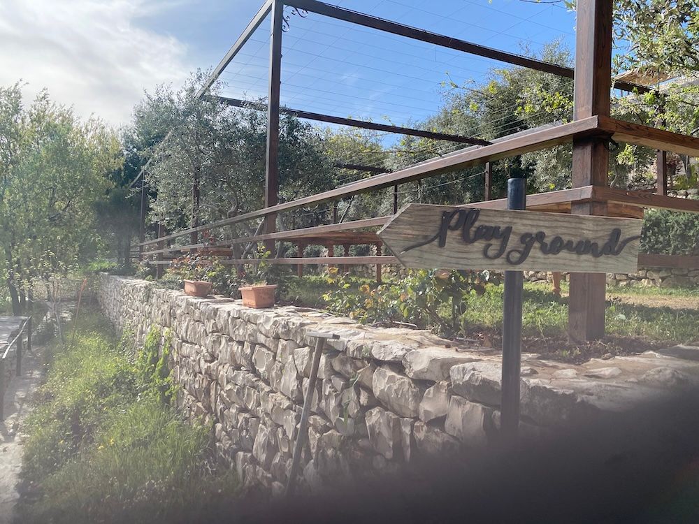 A rustic wooden deck with railings overlooks a stone retaining wall in a sunny garden setting.