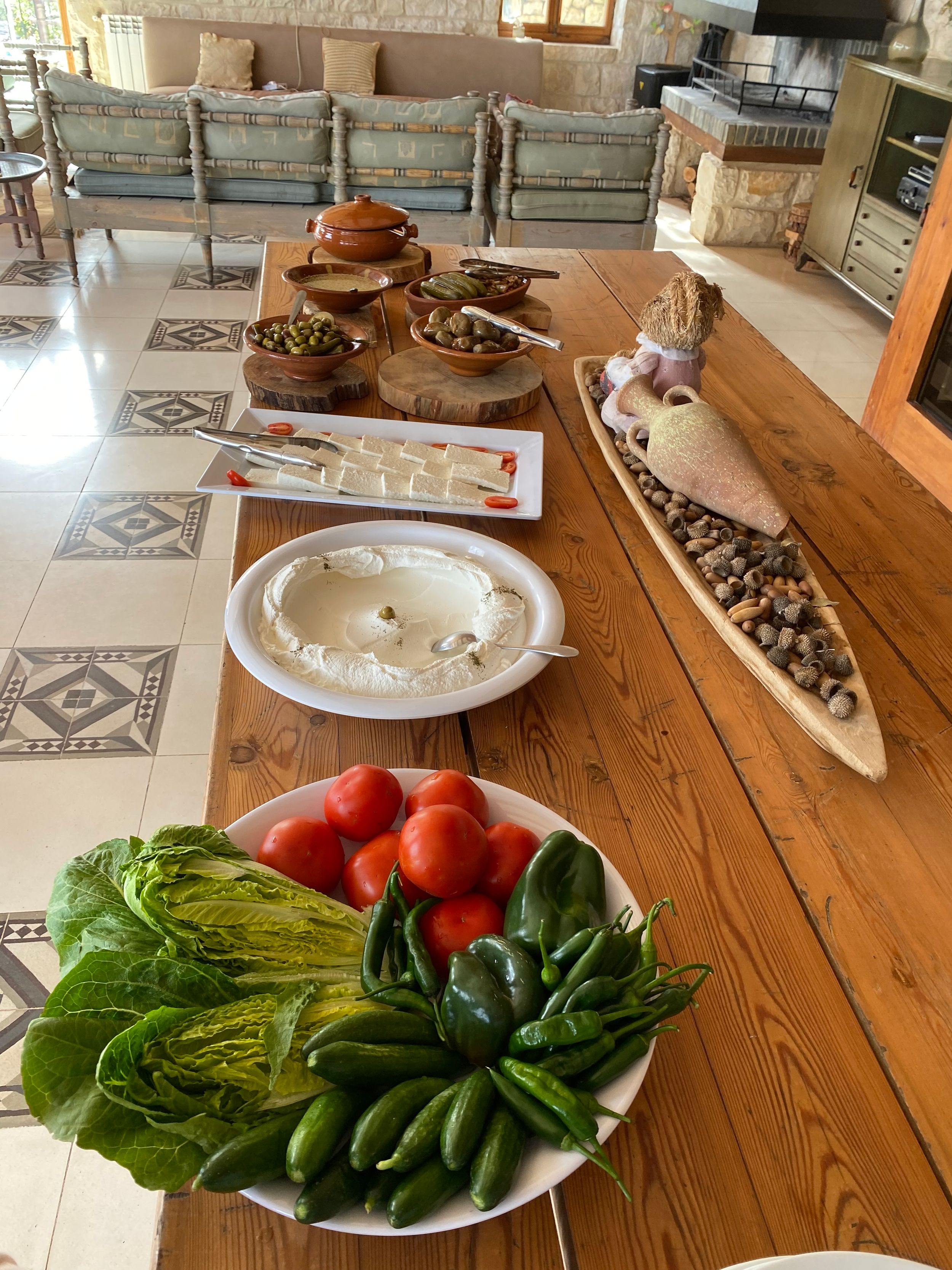 Fresh vegetables including tomatoes and leafy greens displayed on a wooden table with various plates and dishes for serving.