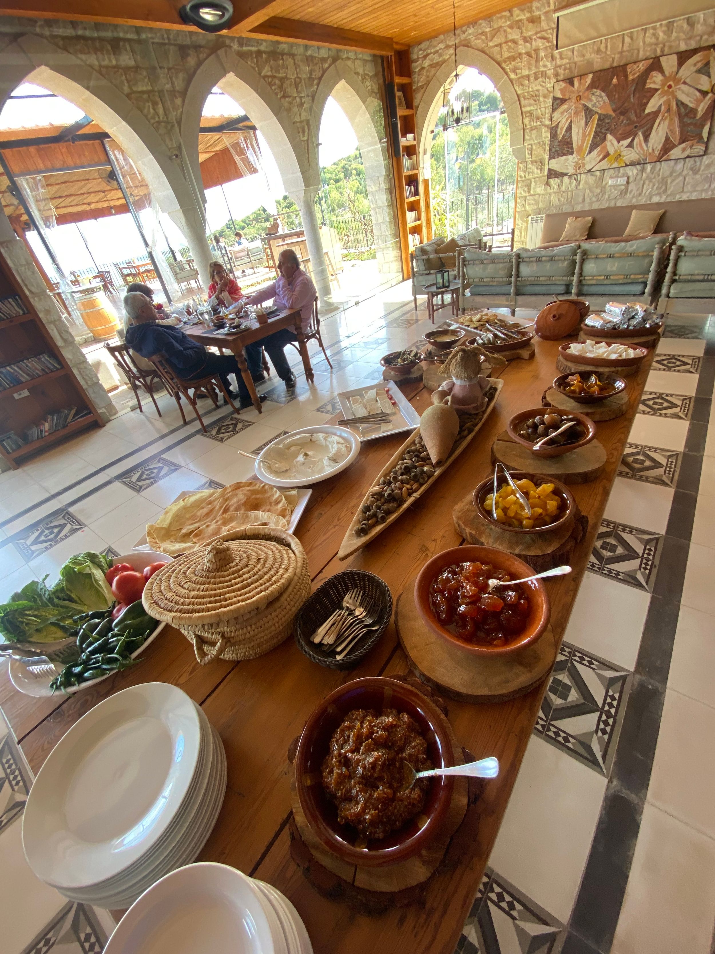 A rustic dining table set with traditional Mediterranean dishes and bowls under stone arches with scenic outdoor views.