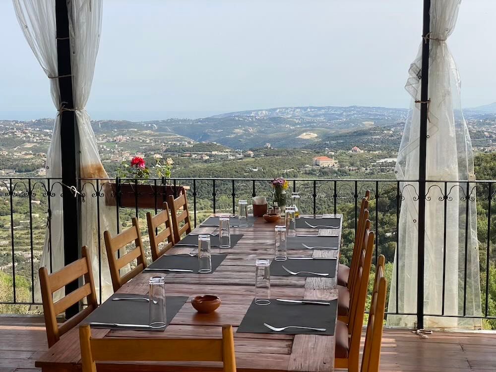 Outdoor dining terrace with tables and chairs overlooking a scenic hillside countryside view.