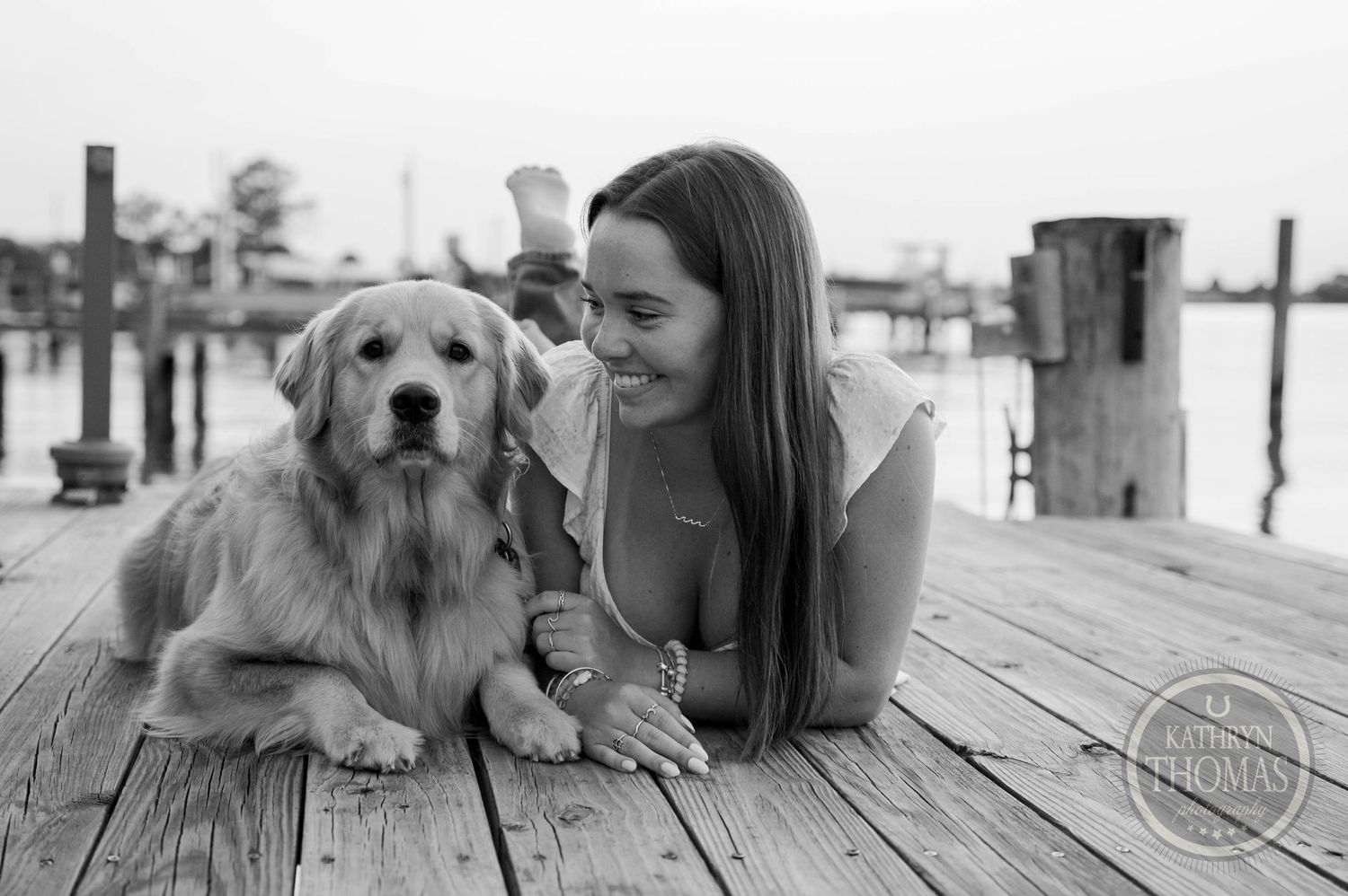 Black and white photo of Golden Retriever and person on dock by marina.