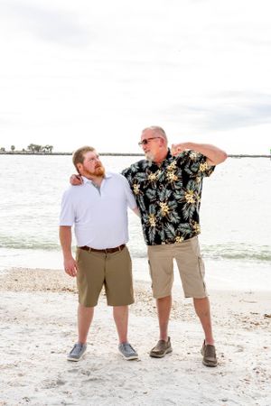 Two people sharing a lighthearted moment on a beach with one wearing a tropical shirt.