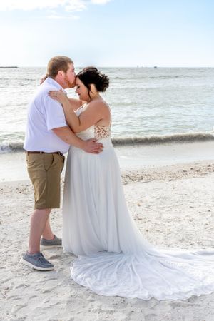 Newlyweds sharing intimate moment on beach with waves in background.