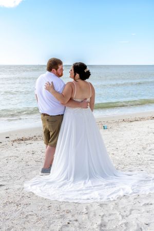 Couple embracing while looking at ocean on sandy beach.