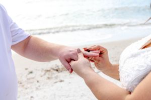 Detailed shot of wedding ring exchange on white sandy beach.
