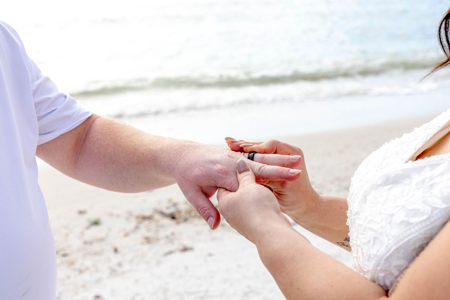 Close-up of wedding ring ceremony on beach with gentle waves in background.