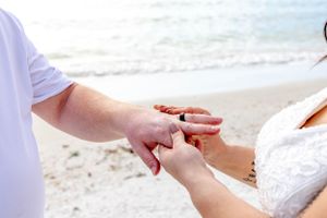 Close-up of hands exchanging rings during beach wedding ceremony.