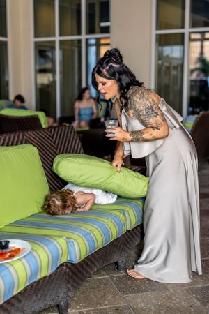 Woman in gray dress with tattoos interacting with someone on striped outdoor couch.