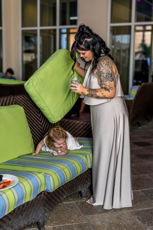 Woman in gray dress holding cushion while standing by outdoor seating area.