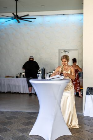 Person in gold dress standing at cocktail table during an event.