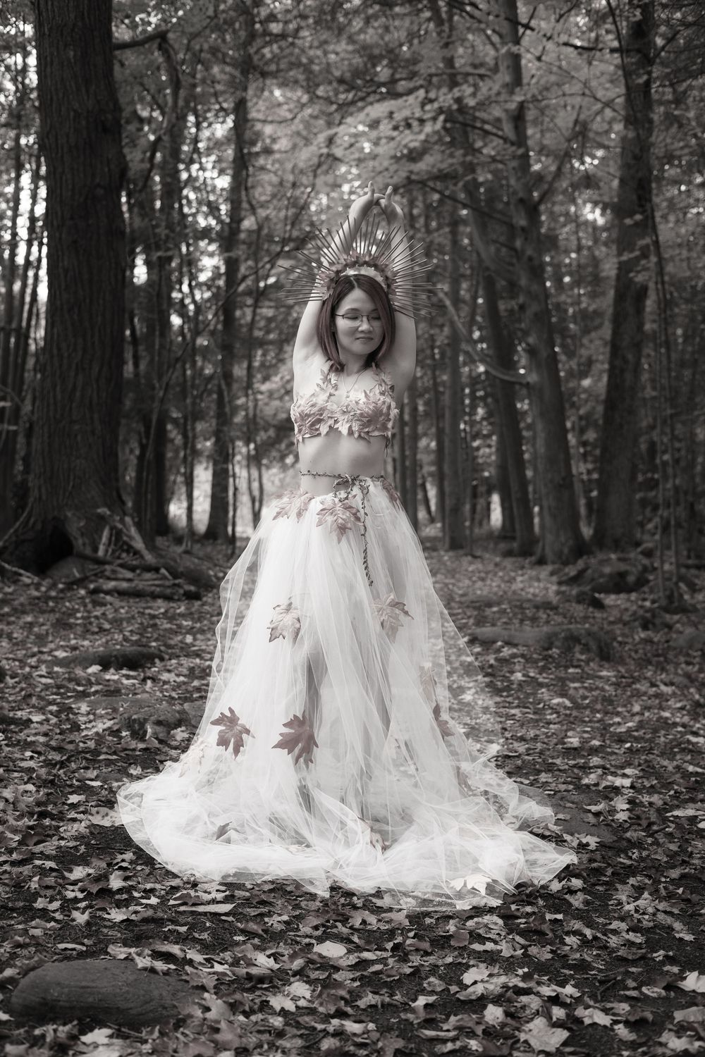 A flowing white lace dress with floral details spreads elegantly across autumn leaves in a misty forest setting.