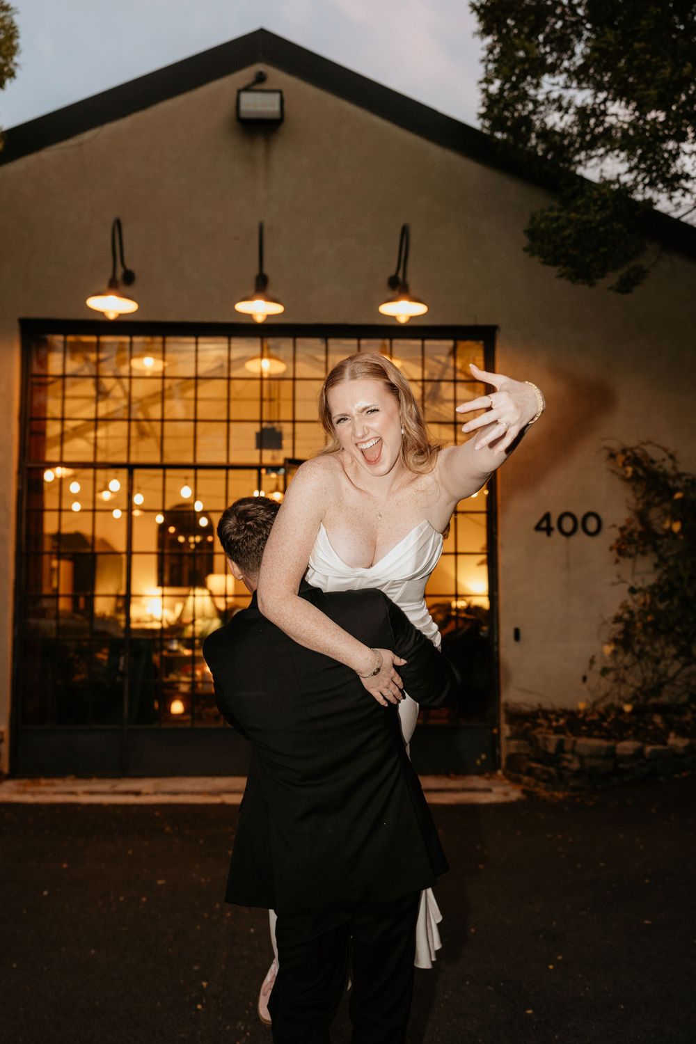Romantic couple embraces outside a warmly lit building with large windows and string lights at dusk at Summerour Studio in Atlanta, Georgia