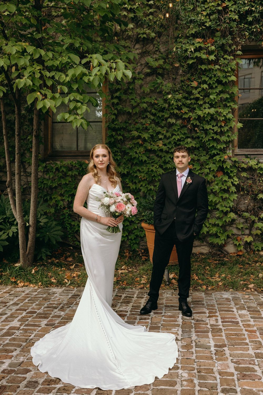 A couple in wedding attire stands on brick pavers in front of a green ivy wall during an outdoor ceremony at Summerour Studio in Georgia