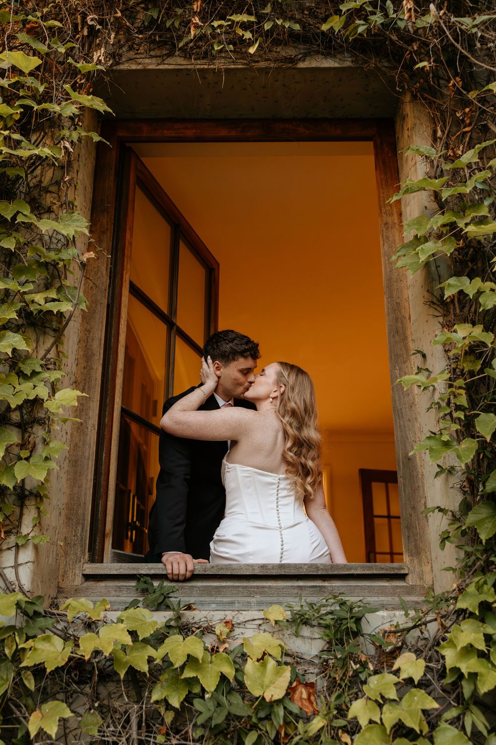 Romantic wedding couple shares intimate moments through an ivy-covered window frame at Atlanta wedding venue, Summerour Studio