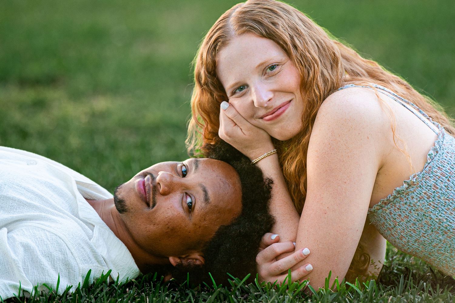 A couple shares intimate moments while laying in the grass during a summer evening.