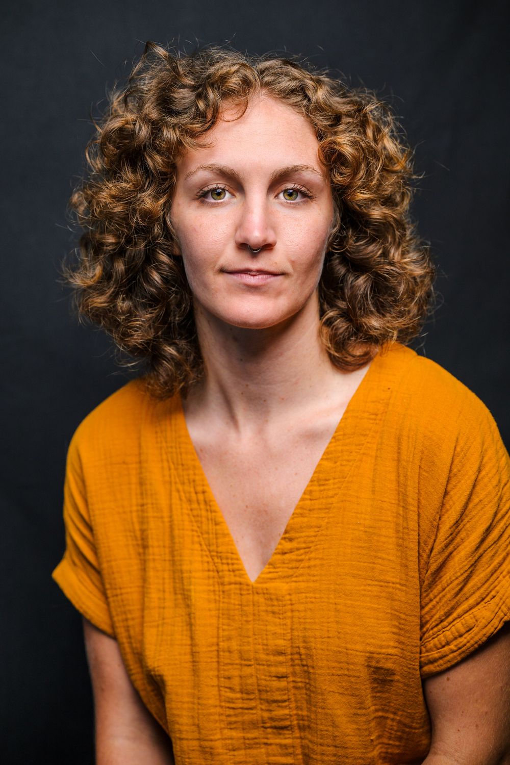 Close-up studio portrait with orange v-neck top against black backdrop.