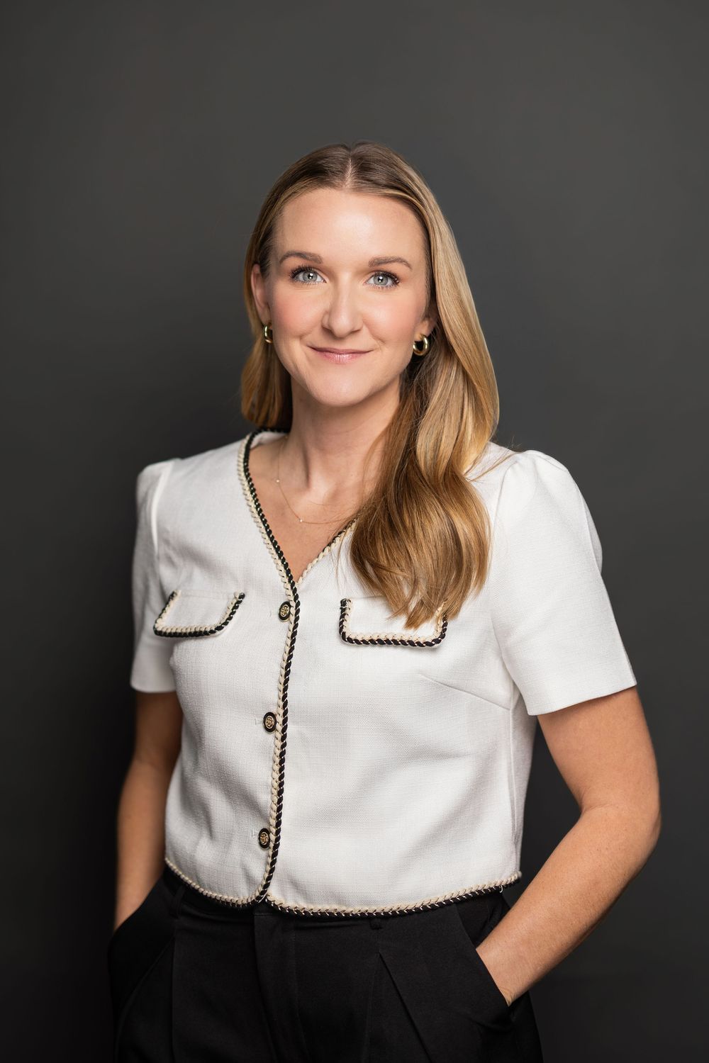 Business casual portrait in white collared top with black trim against charcoal background.