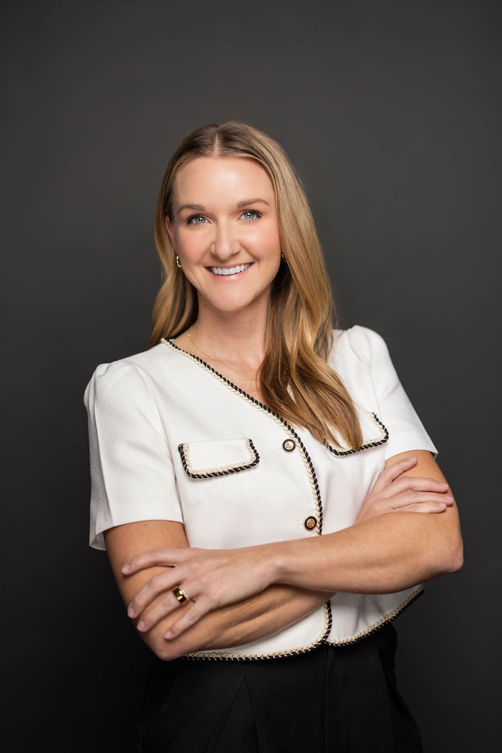 Relaxed studio portrait with arms crossed wearing white top with black piping details.