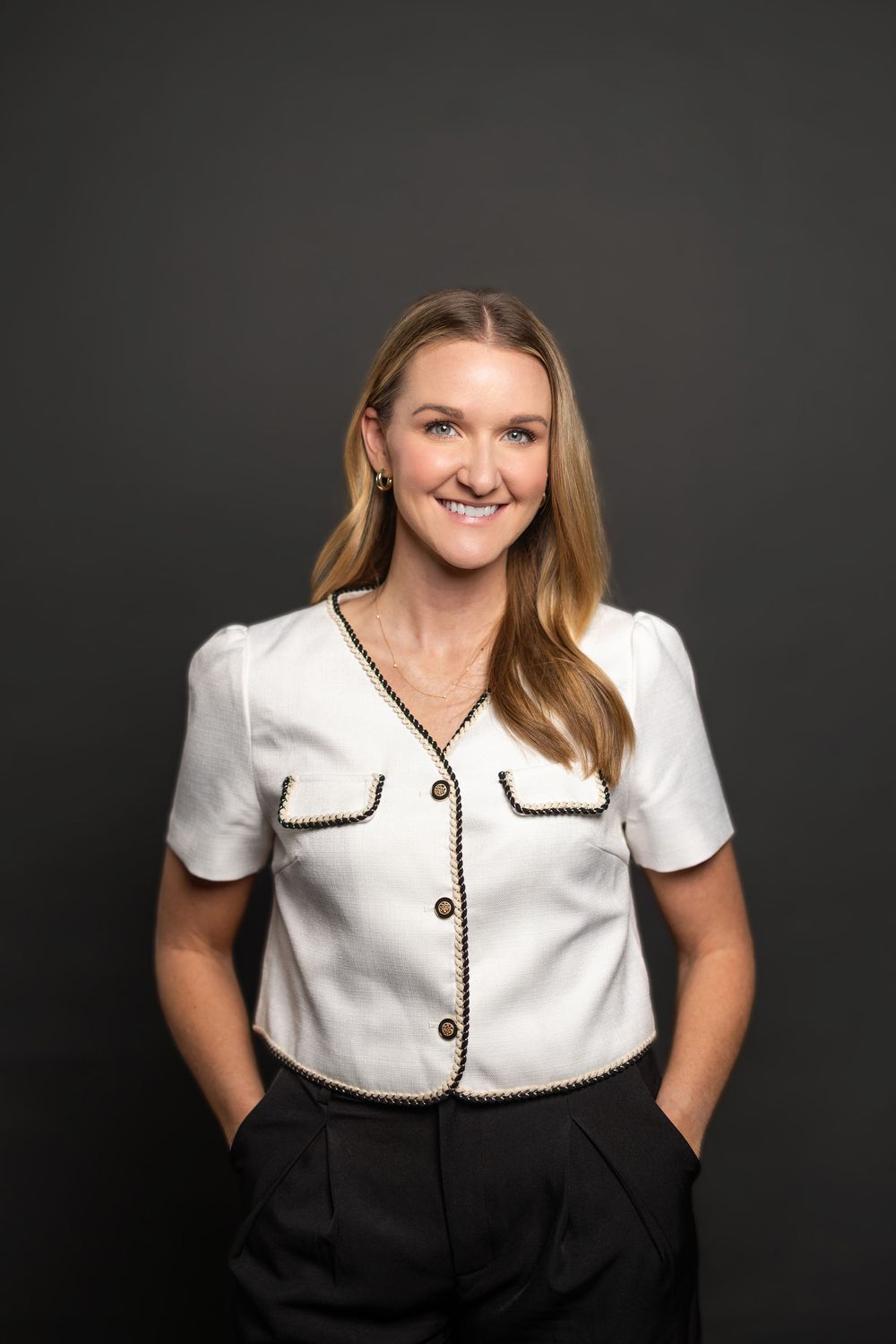 Studio portrait in white collared blouse with black trim against charcoal backdrop.