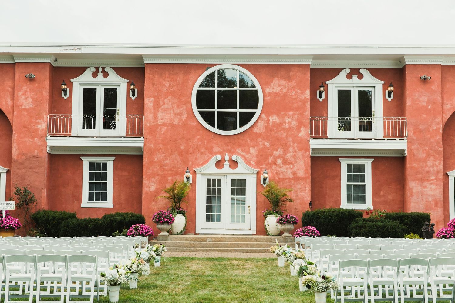 Panoramic view of an outdoor wedding venue with white chairs and a red brick building backdrop.