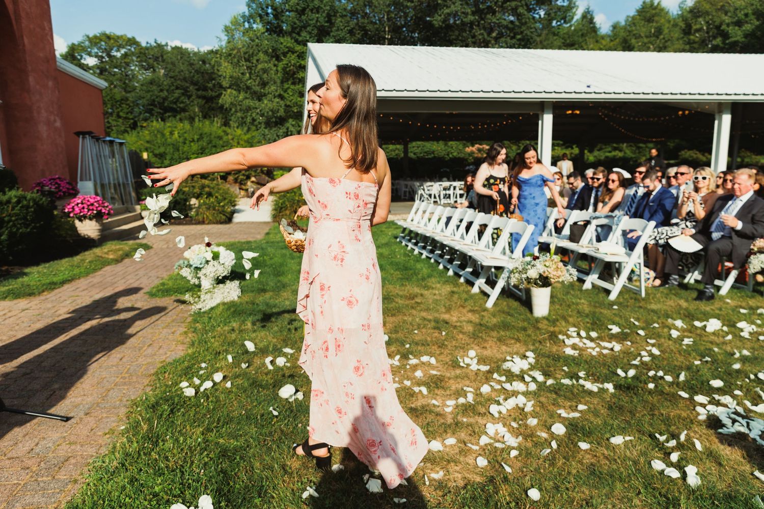 Outdoor wedding reception setup with scattered flower petals and white chairs on a lawn.