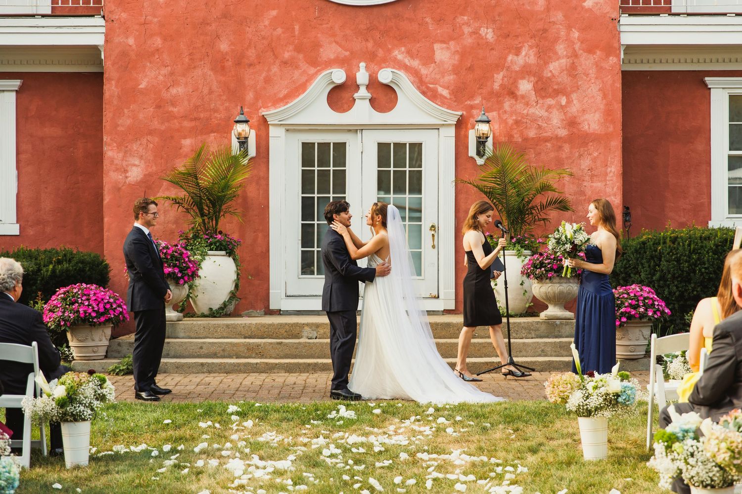 Wedding ceremony in progress at an elegant venue with coral walls and white architectural details.