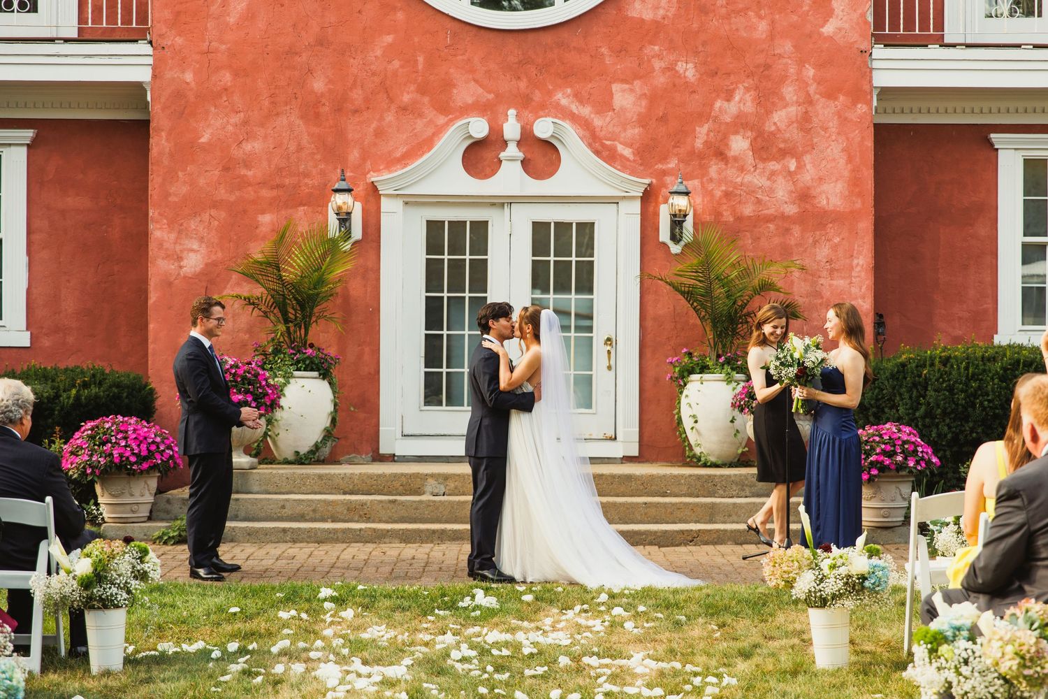 Wide shot of wedding ceremony taking place in front of historic coral-colored building.